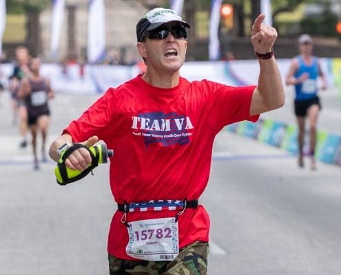 Runner crosses 2019 Austin Half Marathon finish line wearing an American flag SPIbelt. SPIbelt returns as the Official Race Belt of the 2020 Ascension Seton Austin Marathon.