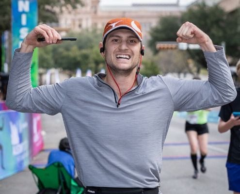 Runner flexes arms while listening to music after he crosses the 2019 Austin Half Marathon finish line. Read this blog and listen to the 10 most recent January running playlist additions.