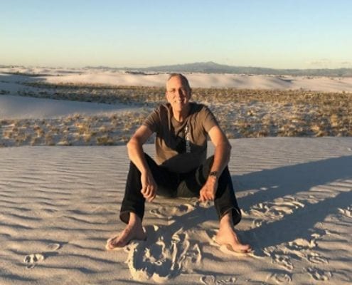 Image of Joe Priesnitz sitting on a sand dune. Joe booked live music acts for the Austin Marathon and 3M Half Marathon before his passing on April 25, 2020. Courtesy of Barbara Nadalini Priesnitz.