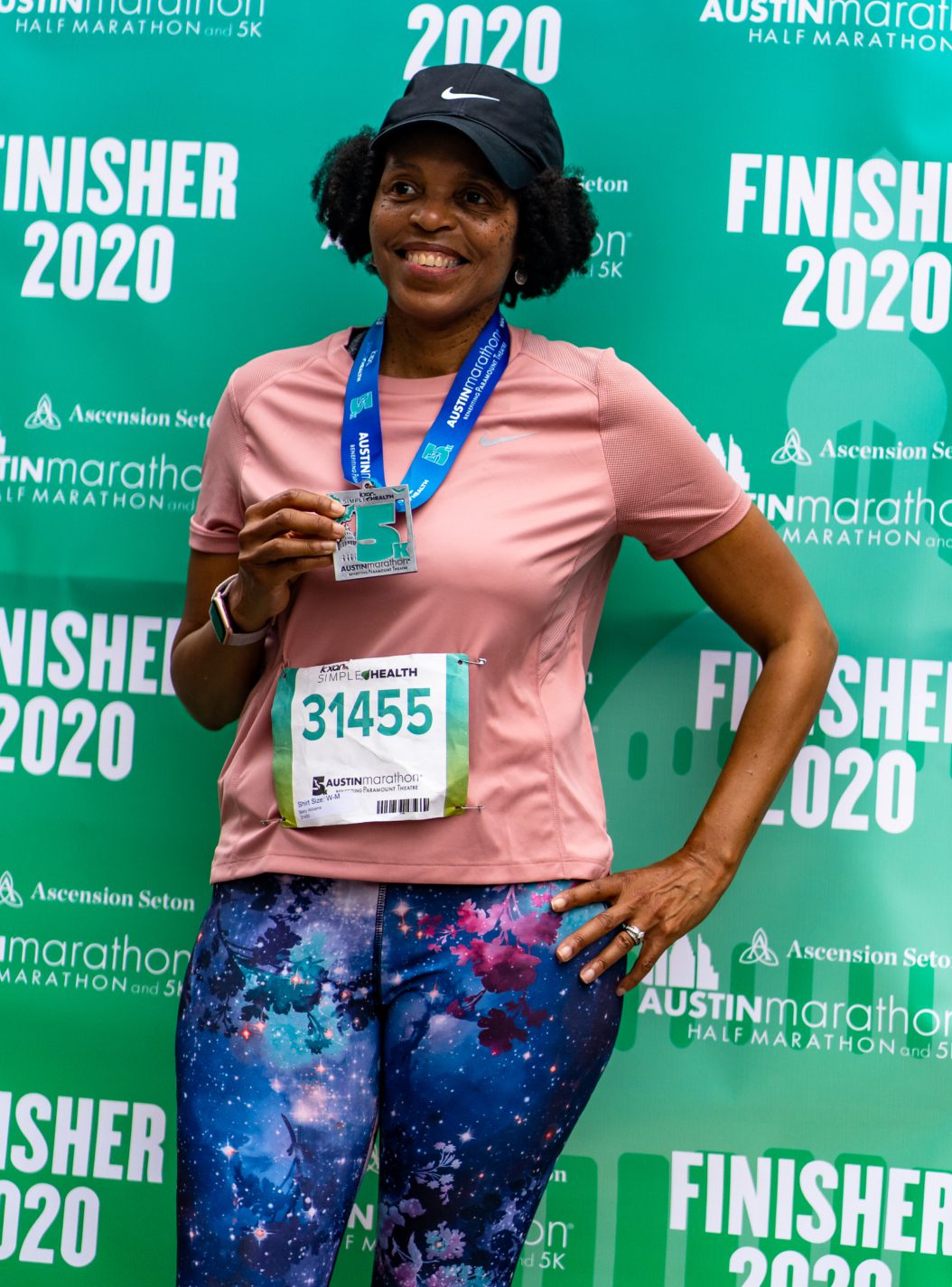 Image of a runner posing in front of a 2020 Finisher backdrop after completing the 2020 KXAN Simple Health 5K. First-time runners should set a goal and find a corresponding training plan, like the free 5K training plan in this blog.