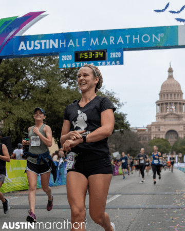 Female runner smiles as she crosses the 2020 Austin Half Marathon finish line.