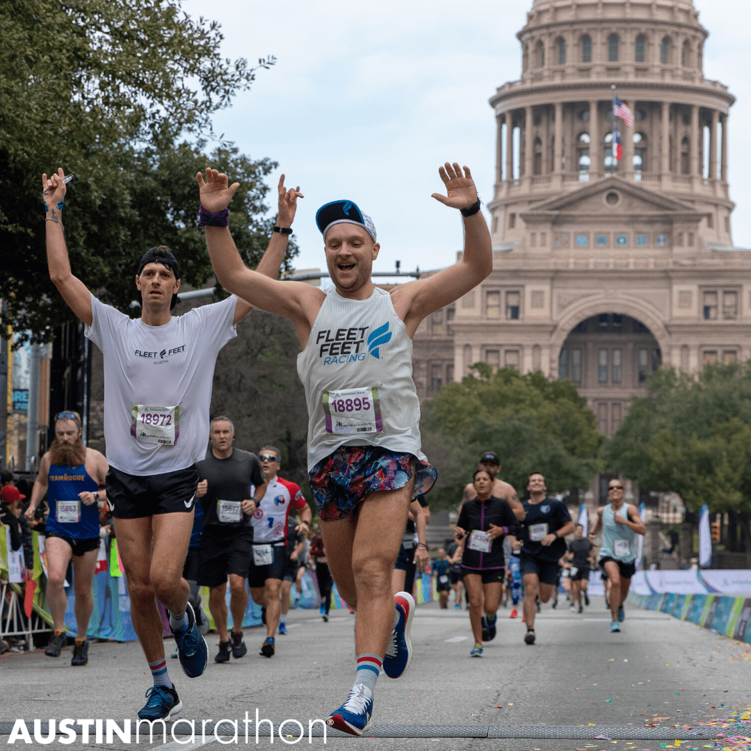 Two runners jump for joy with their hands raised in the air as they cross the 2020 Austin Half Marathon finish line.