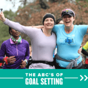 Two women happily stand side-by-side with their arms in the air during the 2020 Ascension Seton Austin Marathon. Text on design reads The ABCs of Goal Setting. Learn more at http://48d.435.myftpupload.com/goal-setting/