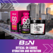 Image of two Bare Performance Nutrition products with a cityscape background. The products, "Go Gel, Mixed Berry" in a pink and black box and "Electrolytes" in a black tub, are showcased. Text below reads: "BPN - Official On-Course Hydration and Nutrition for the Ascension Seton Austin Marathon. Austin Marathon Half Marathon & 5K