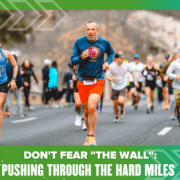 A group of runners participating in a marathon on a paved road, with the main focus on a middle-aged man in a blue long-sleeve shirt and red shorts. The image has a green border with the text "DON'T FEAR 'THE WALL'; PUSHING THROUGH THE HARD MILES" at the bottom. Austin Marathon Half Marathon & 5K