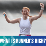 A smiling woman with red hair is running with her arms raised in celebration, likely experiencing the runner's high. She is wearing a white sleeveless top. Other runners are partially visible in the background. Text at the bottom of the image reads, "What is runner’s high? Austin Marathon Half Marathon & 5K