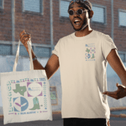 Sporting your exclusive race swag, a person in sunglasses and a beige "Run Austin 2025" t-shirt clutches the matching tote bag. With vibrant Texas imagery and "Austin Marathon" text, they're ready for race day against the backdrop of a brick building and pavement. Austin Marathon Half Marathon & 5K