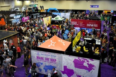 A busy convention hall filled with people walking between colorful booths and displays, including a large orange tent with “Mark the Map” and a purple and white map graphic in the foreground, invites attendees to become a sponsor and join the excitement. Austin Marathon Half Marathon & 5K