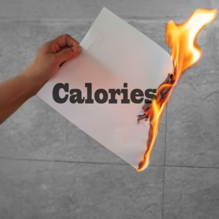 A hand holds a sheet of paper labeled "Calories," with one corner burning—flames consuming part of the text—symbolizing how a calories burn calculator tracks your progress. The background is a gray, tiled wall. Austin Marathon Half Marathon & 5K