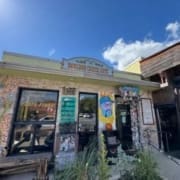 A colorful, eclectic café exterior with a sign reading "Bouldin Creek Café." Art decorates the brick walls beneath a bright blue sky. Green plants grow in front, making it a standout among healthy Austin restaurants. Austin Marathon Half Marathon & 5K