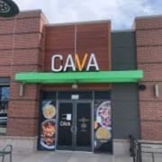 The exterior of a CAVA restaurant with a green awning, brick walls, and large “CAVA” letters above the entrance stands out as a go-to spot for Healthy Austin Restaurants seekers. Food images are displayed on the glass doors. Austin Marathon Half Marathon & 5K