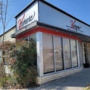 A corner view of Koriente, one of the top healthy dining Austin spots, with large windows, red and black trim, a sign out front, lush plant growth beside the building, and a clear blue sky above. Austin Marathon Half Marathon & 5K