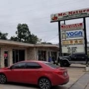 A red car is parked in front of Mr. Natural, a healthy dining Austin spot that serves as a restaurant, bakery, and health food store. The stone exterior and large sign advertise yoga, pastries, and more. Austin Marathon Half Marathon & 5K
