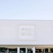 The exterior of a modern white building with large windows and a square sign in the center displaying "PICNIK" in raised letters—a standout among healthy Austin restaurants. The sky above is clear and blue. Austin Marathon Half Marathon & 5K