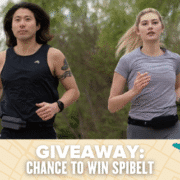 Two people are jogging outdoors, wearing SPIBELT running belts. Text at the bottom reads, "GIVEAWAY: CHANCE TO WIN SPIbelt" on a patterned background with doodles, announcing an exciting SPIbelt giveaway. Austin Marathon Half Marathon & 5K