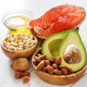 A variety of healthy foods, ideal for a runner’s diet, including a raw salmon steak, half an avocado, olive oil, cashews, almonds, hazelnuts, and a walnut—all arranged on a white wooden surface. Austin Marathon Half Marathon & 5K