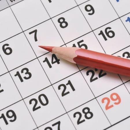 A red pencil rests on a calendar page, pointing at the 14th day of the month. The dates are arranged in a grid, with Recovery days and the number 29 highlighted in red. Austin Marathon Half Marathon & 5K