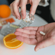 A person pours a white capsule from a pill bottle into their hand, with an orange half and various blister packs of pills nearby—highlighting common runners nutrition practices and potential nutrition myths. Austin Marathon Half Marathon & 5K
