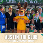 A group of smiling athletes pose together under an Austin Tri Club tent in Austin, joined by Buck the deer mascot. Text below reads: "Austin Tri Club – Free Group Run. Austin Marathon Half Marathon & 5K