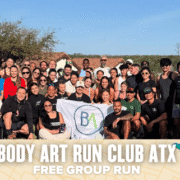 A large, diverse group of people pose together outdoors, smiling and holding a "BA" flag. Below them, text reads: "Body Art Run Club ATX - Free Group Run." Join Body Art’s welcoming ATX run club with trees and rooftops in the background. Austin Marathon Half Marathon & 5K