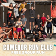 A diverse group of runners from Comedor Run Club poses and smiles outdoors, some standing, others sitting or playfully hanging from scaffolding. A banner below announces a free group run with colorful, decorative graphics. Austin Marathon Half Marathon & 5K