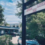 A coffee shop building with a sign in the foreground that reads "EPOCH LOVES YOU." Popular among post-run cafés and Austin coffee lovers, cars are parked outside and trees surround the area under a blue sky. Austin Marathon Half Marathon & 5K