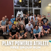 A diverse group of smiling runners poses outside a building, some sitting on picnic benches and others standing behind. A banner at the bottom reads "Plant Powered Athlete Free Group Run," highlighting this inclusive group run event. Austin Marathon Half Marathon & 5K