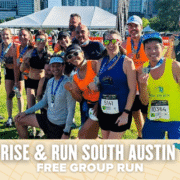 A group of smiling runners, wearing Rise & Run South Austin medals and race bibs, pose together outdoors after a run. The text below reads "RISE & RUN SOUTH AUSTIN FREE GROUP RUN." City buildings and event tents are in the background. Austin Marathon Half Marathon & 5K
