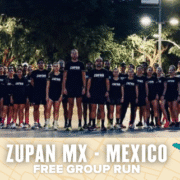 A large group of people in matching black "ZUPAN" shirts pose outdoors at dusk under streetlights. Text overlay at the bottom reads, "ZUPAN MX - MEXICO FREE GROUP RUN," celebrating a spirited ZUPAN MX free run event. Austin Marathon Half Marathon & 5K