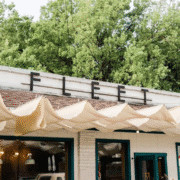 A white building with teal window frames features a black sign on the roof that reads "FLEET." Beige awnings hang over the entrance, and green trees are visible in the background—an inviting Austin spot for post-run cafés or morning coffee. Austin Marathon Half Marathon & 5K