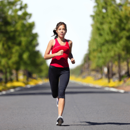 A woman in a red tank top and black leggings is running on a paved road lined with green trees, preparing her mind for race day under the clear sky. Austin Marathon Half Marathon & 5K