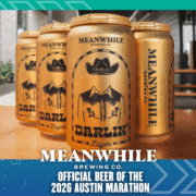Four gold cans of Meanwhile Brewing Co.'s Darlin' Lager are arranged on a table. Text below announces Meanwhile Brewing Co. as the Official Beer of the 2026 Austin Marathon. Austin Marathon Half Marathon & 5K