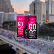 Two boxes of BPN GO GEL Endurance Gel, Mixed Berry flavor, are displayed in front of a blurred cityscape with a crowd gathered on a bridge—perfect fuel for your next training season and an essential addition to your gear check. Austin Marathon Half Marathon & 5K