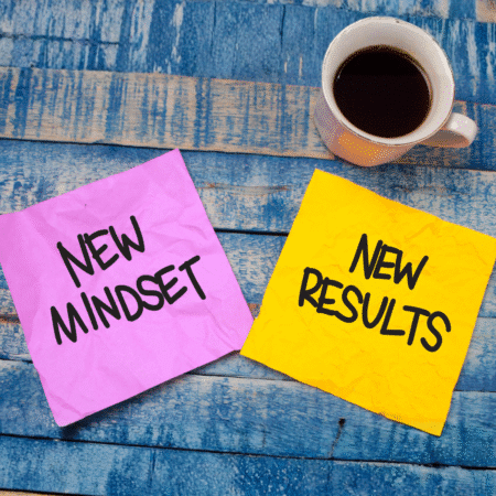 A cup of black coffee sits on a blue wooden surface beside two crumpled sticky notes, symbolizing progress reflection. One pink note reads "NEW MINDSET" and a yellow note reads "NEW RESULTS" in bold black letters. Austin Marathon Half Marathon & 5K