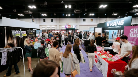 Crowds of people Explore the Expo at the Austin Marathon Expo, walking through a busy hall lined with vendor booths featuring banners, signage, running gear, and products. Some attendees hold bags and interact with exhibitors. Austin Marathon Half Marathon & 5K
