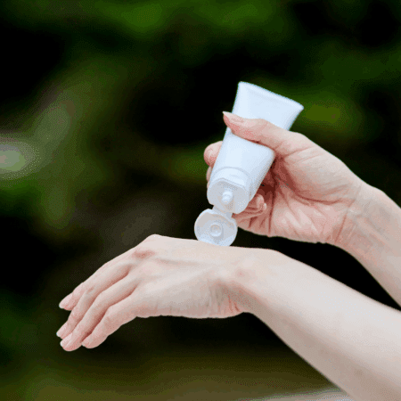 A person holds a white tube and squeezes lotion or cream onto the back of their other hand—an important step among race day essentials for the Austin Marathon, set against a blurred green background. Austin Marathon Half Marathon & 5K