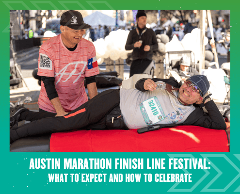 A smiling man in running gear lies on a red massage table as another man massages his leg at the Austin Marathon Finish Line Festival, celebrating amid the lively crowd and festive tents in the background. Austin Marathon Half Marathon & 5K