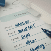 A close-up of a handwritten daily schedule shows tasks: wake up at 6:00, breakfast, gym at 8:00, plus prep for a 5K. Office and shopping are listed next. A pen and file folder rest nearby. Austin Marathon Half Marathon & 5K