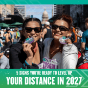Two women in athletic clothes smile and hold up medals at a busy outdoor race event. The text reads: "5 signs you’re ready to level up your distance for 2027." The Texas Capitol building rises in the background. Austin Marathon Half Marathon & 5K