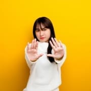 A woman in a white sweater stands against a bright yellow background, holding both hands forward with palms facing out as if signaling to stop—her serious expression reflecting the need for mental recovery. Austin Marathon Half Marathon & 5K