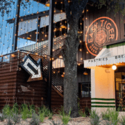 A modern building with a large "Easy Tiger Bake Shop & Beer" sign, string lights, and a patio—one of the best Austin patio spots for runners to relax after enjoying spring in Austin. A tree and landscaping sit in the foreground by the white “PASTRIES BREAD” awning. Austin Marathon Half Marathon & 5K