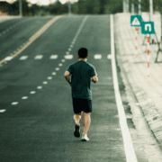A person in athletic clothes jogs alone on an empty road, likely focused on base building for marathon training, with road signs ahead and trees in the background. The calm scene suggests early-morning running preparation. Austin Marathon Half Marathon & 5K