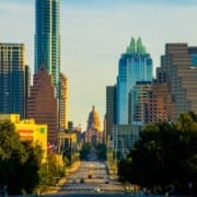 Downtown Austin, Texas skyline at sunset with the Texas State Capitol centered and modern buildings flanking a tree-lined street—one of the top running routes for spring running enthusiasts exploring scenic Austin running routes. Austin Marathon Half Marathon & 5K