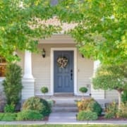 A well-maintained house entrance with a dark gray door decorated with a floral wreath, surrounded by lush green bushes and sunlit foliage—typical charm found in Austin neighborhoods along the marathon route. Steps and a walkway lead to the front porch. Austin Marathon Half Marathon & 5K