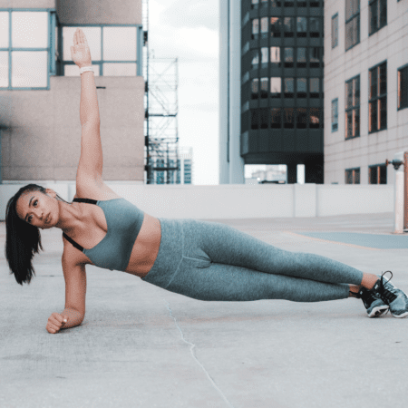 A woman in athletic wear performs a side plank exercise on a rooftop, showcasing strength training for runners with her impressive performance, surrounded by the tall buildings of the city. Austin Marathon Half Marathon & 5K