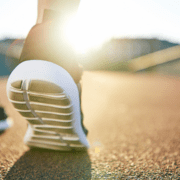 Close-up of a person’s running shoe as they jog on a sunlit outdoor track, highlighting the dedication to marathon training with sunlight shining brightly in the background. Austin Marathon Half Marathon & 5K