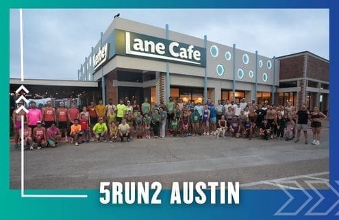 A large group of runners from the Buda Running Club pose together outside Lane Cafe at dawn or dusk, with "5RUN2 Austin" in bold white letters at the bottom. The scene features a blue and teal border with arrow graphics. Austin Marathon Half Marathon & 5K