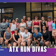 A group of women runners, some holding dogs, pose and smile outside a storefront with large windows after an ATX Run Divas group run. Text at the bottom reads "ATX RUN DIVAS" on a purple and blue gradient background. Austin Marathon Half Marathon & 5K