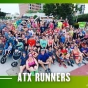 A large, diverse group of runners from the Buda Running Club poses together outdoors on a city sidewalk. Some have strollers, and all wear athletic clothing. The text "ATX RUNNERS" is displayed at the bottom of the image. Austin Marathon Half Marathon & 5K