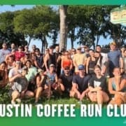 A large group of smiling people in athletic wear pose together outdoors in front of a Batch sign, with trees in the background, after a Group Run. Text at the bottom reads, "Austin Coffee Run Club. Austin Marathon Half Marathon & 5K